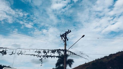 Low angle view of electricity pylon against cloudy sky