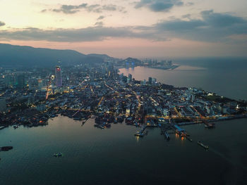 High angle view of illuminated city by sea against sky