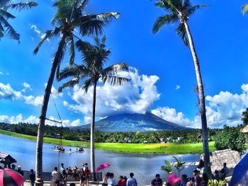 People by palm trees on landscape against blue sky