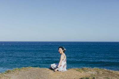 Portrait of young woman sitting by sea on sunny day