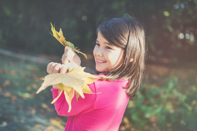 Happy mixed race japanese girl in autumn park holding maple leaves, smiling. sunlight, copy space