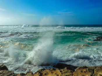 Waves splashing on rocks at shore against sky