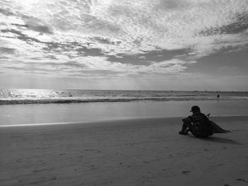 Man sitting on shore at beach against sky