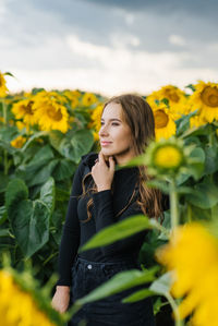 A beautiful young woman in a hat dreams while walking among the sunflower flowers