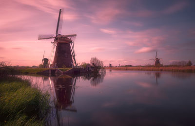 Traditional windmill by lake against sky during sunset