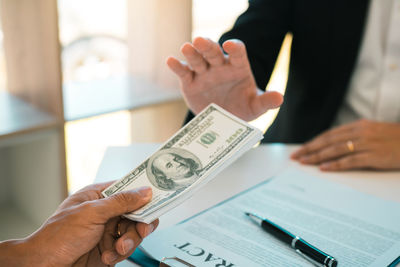 Cropped hands of man giving bribe with business person refusing to accept on table