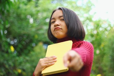 Portrait of teenage girl holding book pointing outdoors