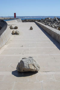 Stones on footpath by sea against clear sky