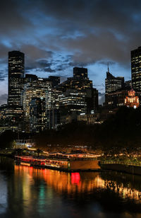 Illuminated buildings by river against sky at night