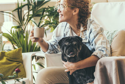 Smiling woman drinking coffee while sitting with dog at home