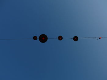 Low angle view of hanging lights against clear blue sky