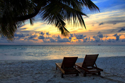 Empty lounge chairs on beach against sky during sunset