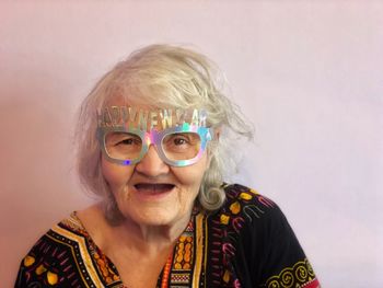 Portrait of senior woman wearing novelty glasses against wall