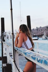 Side view of young woman standing on pier by sea in city