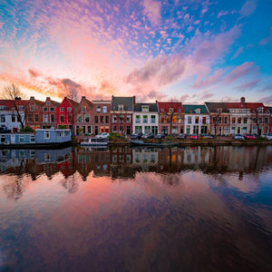 Buildings by river against sky during sunset