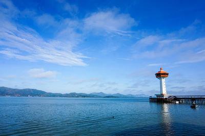 Lighthouse in sea against cloudy sky