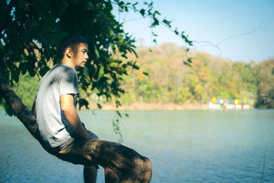 Thoughtful young man sitting on tree by lake