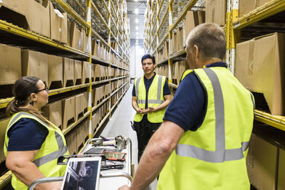 Multi-ethnic coworkers discussing while standing amidst racks at distribution warehouse