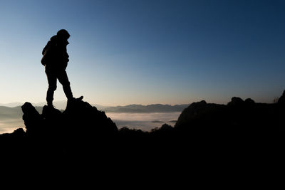 Silhouette man standing on rock against sky during sunset