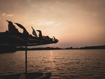 Silhouette man relaxing on boat in sea against sky during sunset