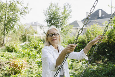 Senior woman holding chain of swing in garden