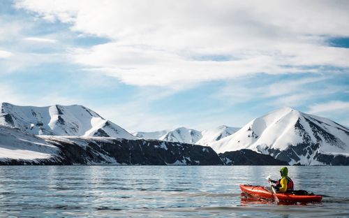 People in boat on river against snowcapped mountains