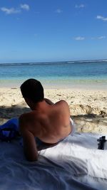 Rear view of shirtless man sitting on beach