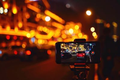 Close-up of smart phone on tripod in illuminated city at night