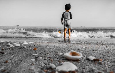 Rear view of boy standing on beach against clear sky