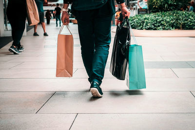 Low section of man with bags walking on sidewalk