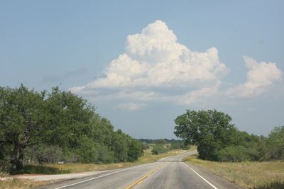 Empty road amidst trees against sky