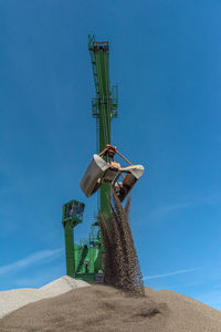 Green harbor crane pours sand and gravel onto a hill