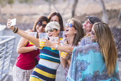 Friends enjoying drinks while taking selfie on beach