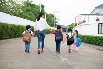 Rear view of woman holding with children while walking on footpath