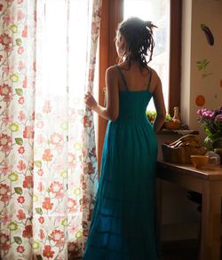 Rear view of young woman looking through window at home