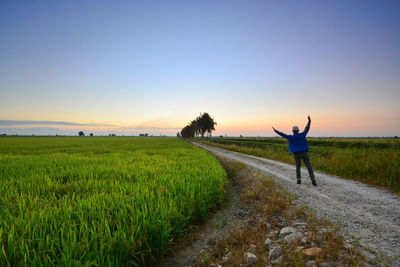 Rear view of man standing on dirt road against clear sky