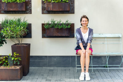 Portrait of smiling young woman sitting on potted plant