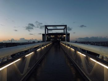 Footbridge over illuminated bridge against sky at sunset