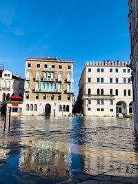 Canal by buildings against clear blue sky