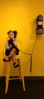 Portrait of young girl sitting on chair holding retro phone. 