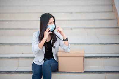 Woman using mobile phone by box on staircase