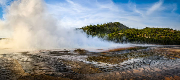 Panoramic view of trees on shore against cloudy sky