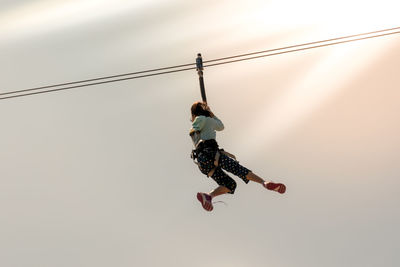 Low angle view of woman zip lining against sky