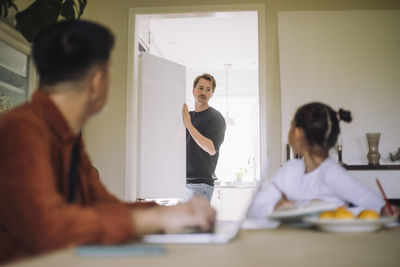 Daughter looking at father standing near refrigerator in kitchen at home