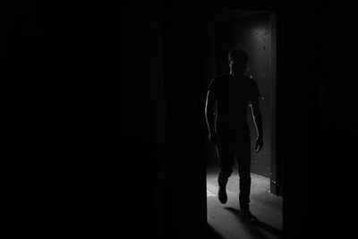 Rear view of silhouette man walking in illuminated corridor