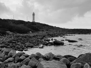 Lighthouse on rocks by sea against sky