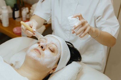 A girl cosmetologist applies a cream mask with a brush to a woman s face.