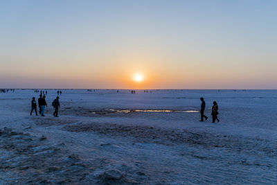 Silhouette people on beach against sky during sunset