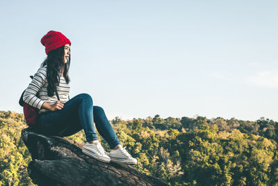 Young woman sitting on tree against sky