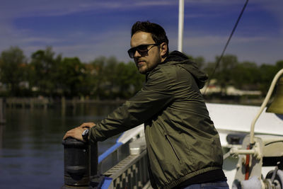 Side view of man wearing sunglasses standing in boat on lake